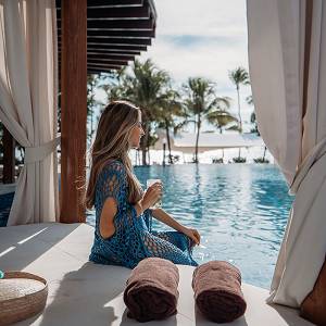 Woman enjoying a drink in a palapa by the pool.